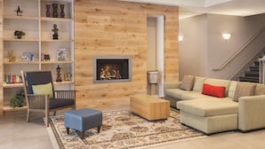 A modern living room with a fireplace, a sectional sofa, a wooden bookshelf, and a patterned rug. - Country Inn & Suites by Radisson, Conyers, GA (Conyers)