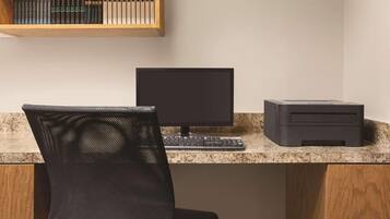 Un espacio de trabajo con computadora, teclado e impresora sobre una encimera de granito, una silla de malla y una estantería arriba.