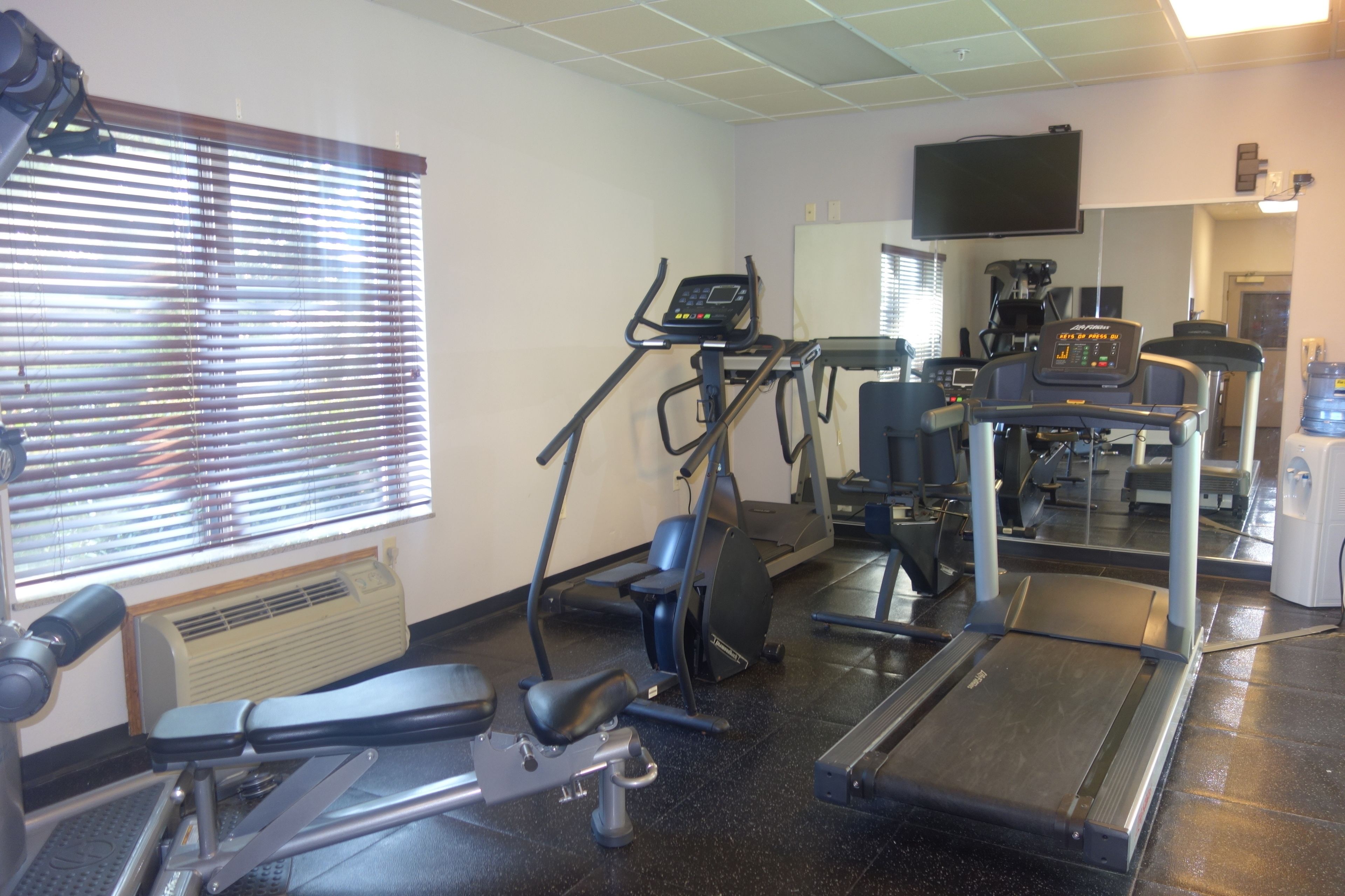 A gym with exercise equipment, a television, and a window with blinds.