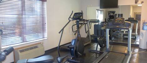 A gym with exercise equipment, a television, and a window with blinds.