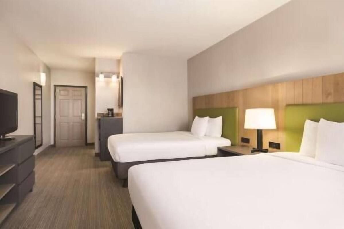 A hotel room with two beds, a television, a desk, and a mirror.