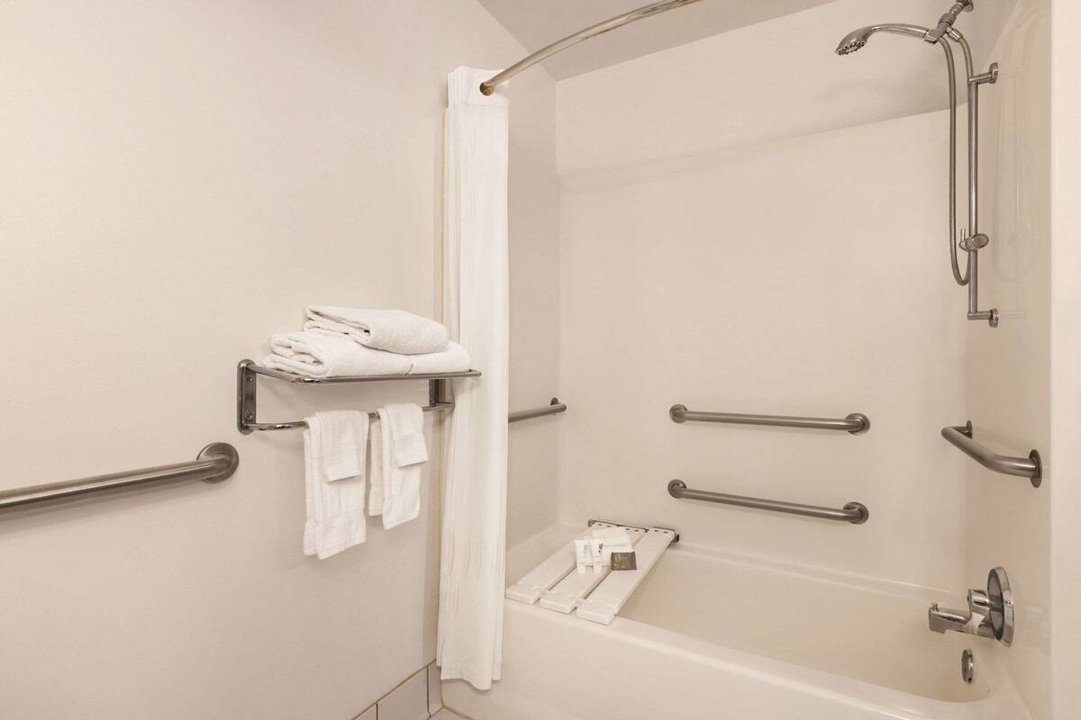A modern bathroom with a bathtub, grab bars, a towel rack, and a shower curtain.
