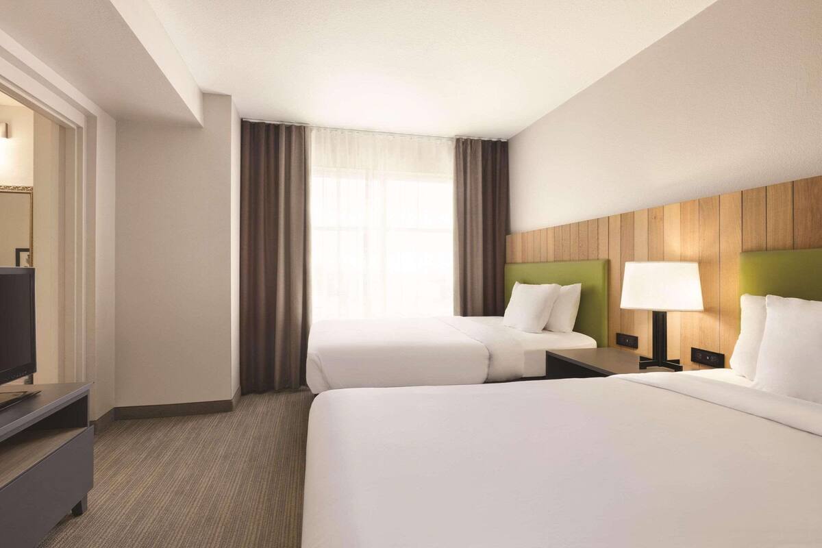 A hotel room with two beds, a television, a desk, and a lamp.