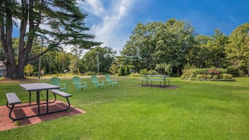 A picnic area with tables and chairs, surrounded by grass and trees.