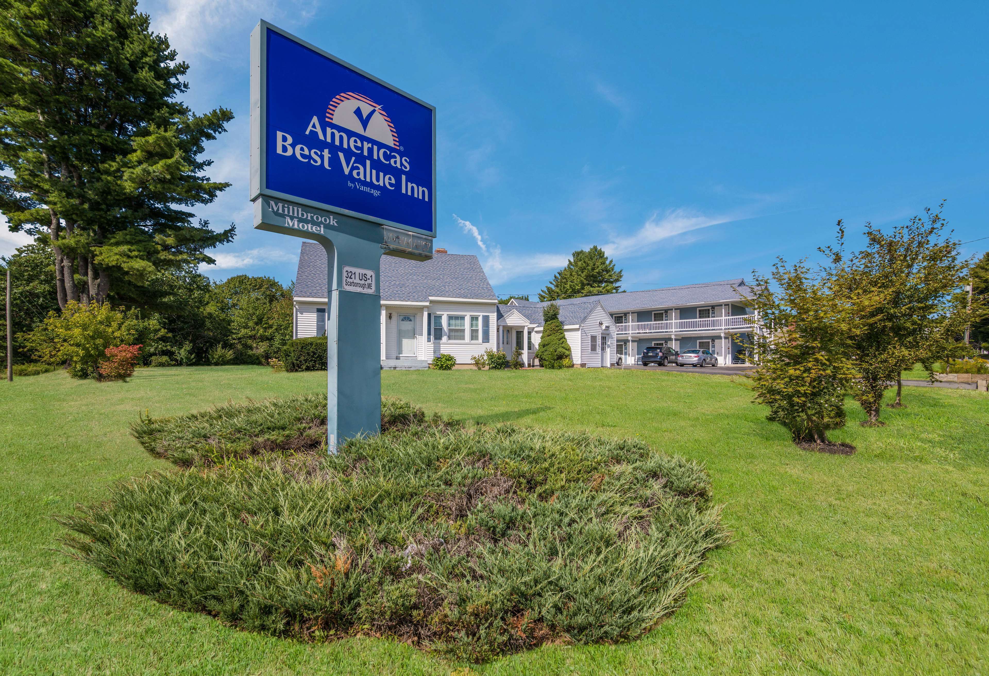 A sign for the Americas Best Value Inn by Vantage, featuring a large blue sign with white lettering, set against a backdrop of a well-maintained lawn and a row of white houses.