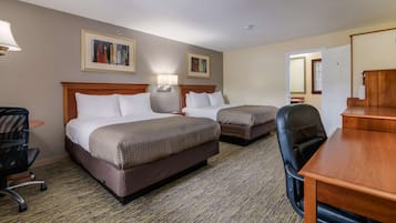 A hotel room with two beds, a desk, a chair, a lamp, and two framed pictures on the wall.