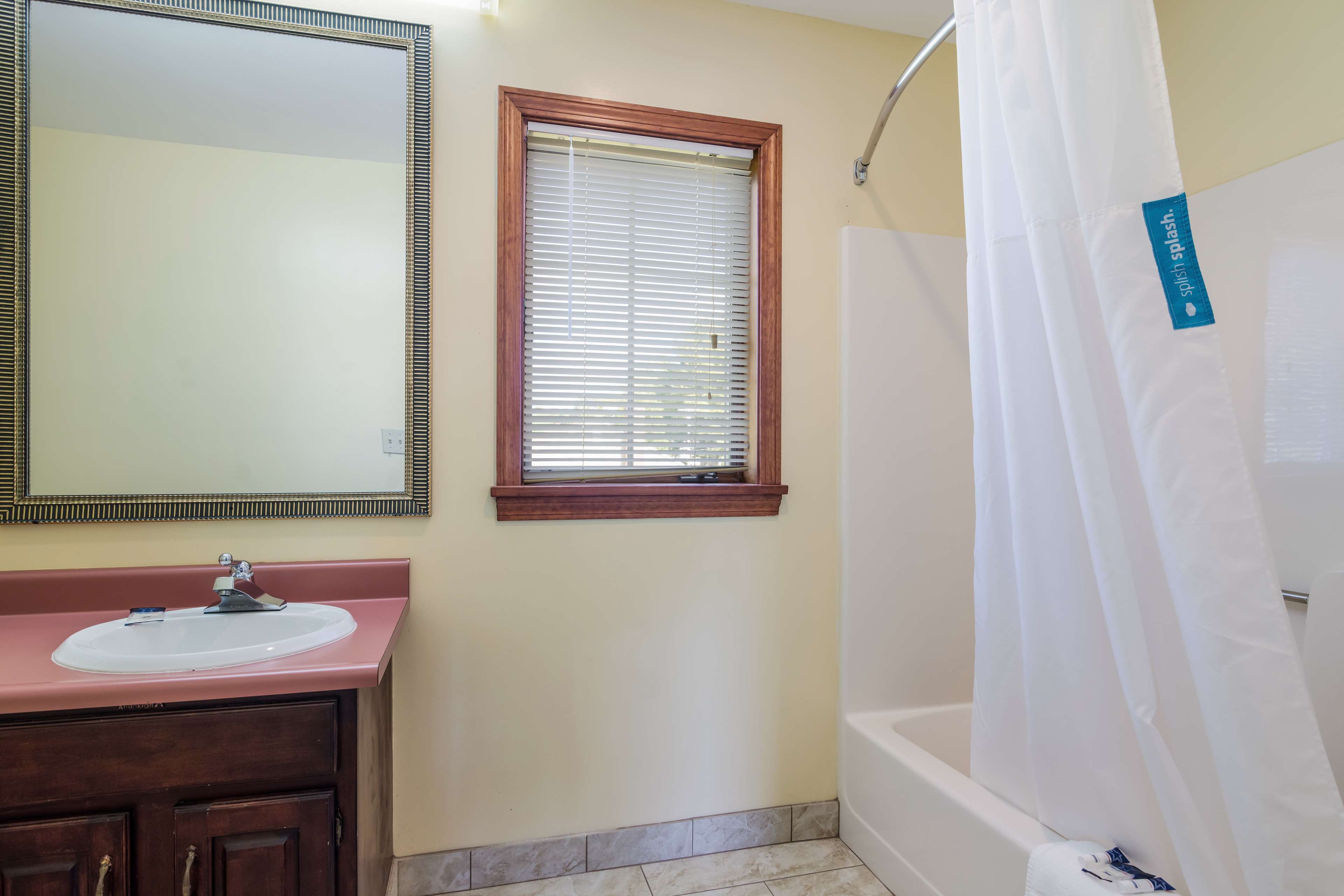 A bathroom with a sink, mirror, window, and shower.