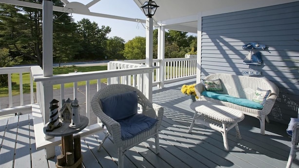 A covered porch with white railings, wicker furniture, and a small lighthouse model. - Americas Best Value Inn Scarborough Portland (Scarborough)