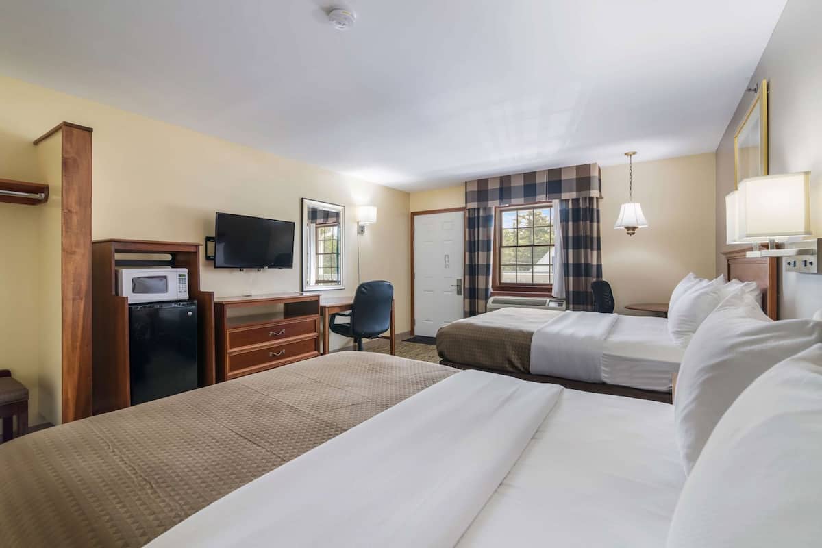 A hotel room with two beds, a desk with a TV, a microwave, and a chair.