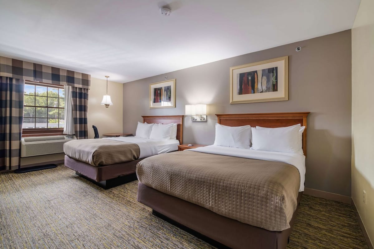 A hotel room with two beds, a window with curtains, a wall-mounted lamp, and a framed picture.