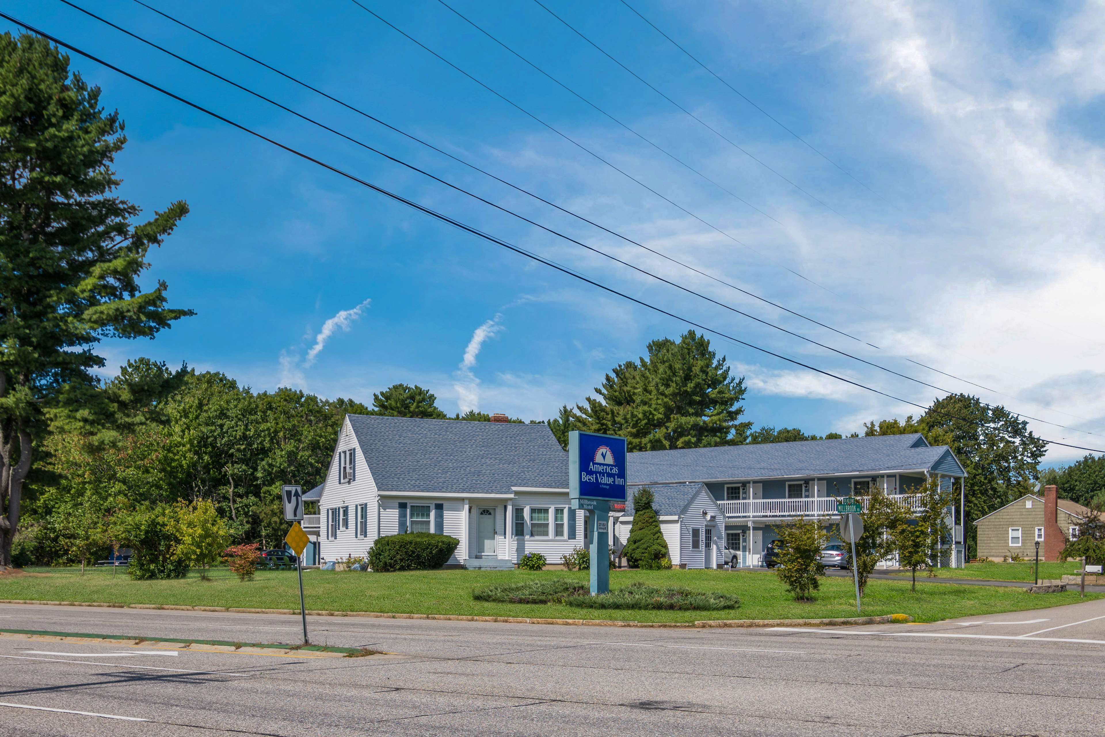 A two-story motel with a blue sign, a grassy lawn, and a clear sky.