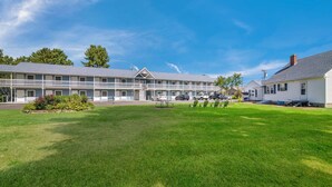 A motel with a front lawn, multiple cars parked in front, and a clear blue sky. - Americas Best Value Inn Scarborough Portland (Scarborough)