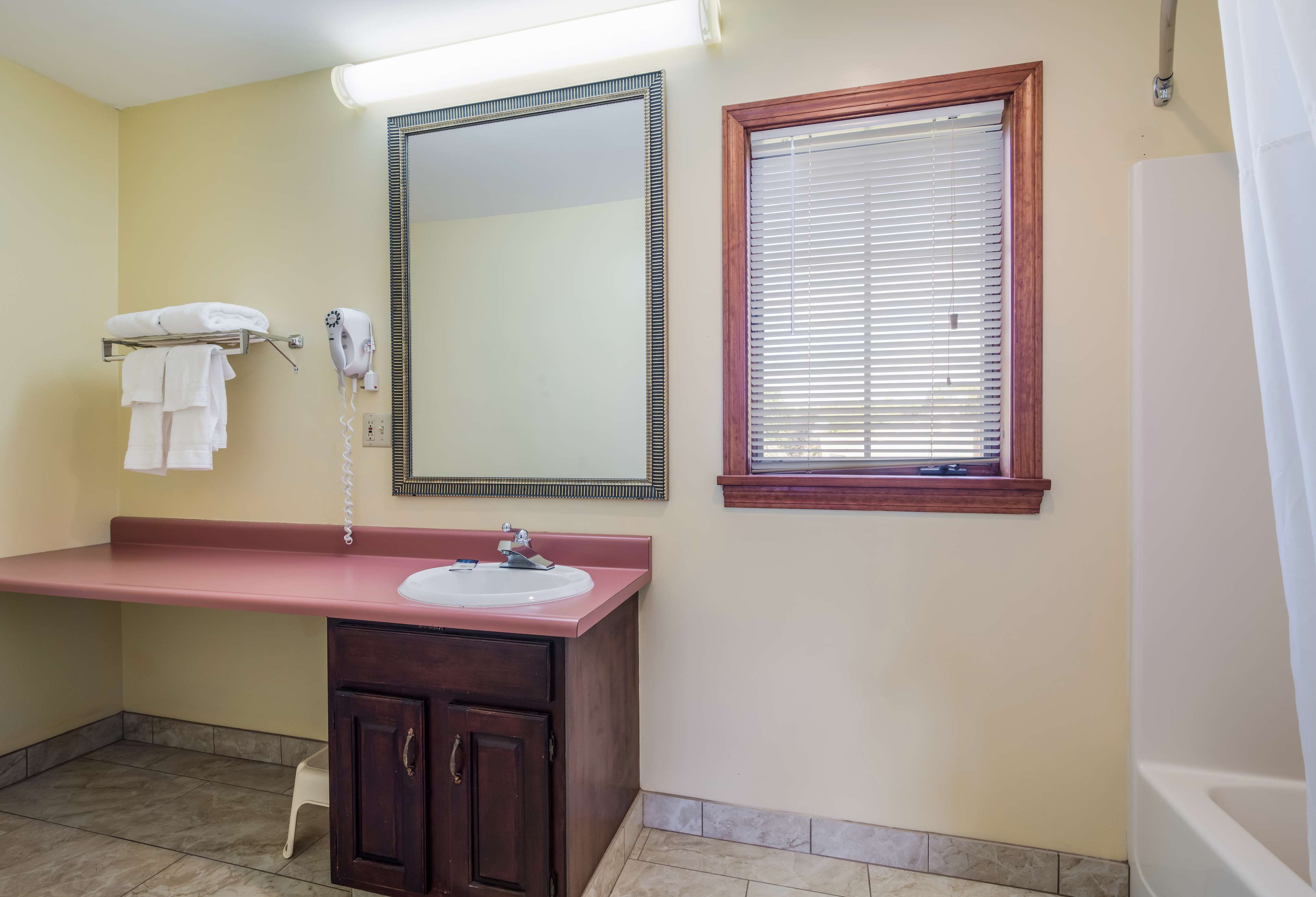 Un baño con lavamanos, espejo, toallero y ventana.