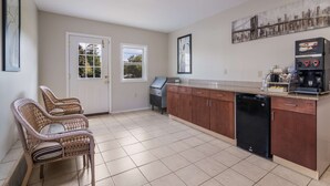 A kitchen with a dishwasher, a coffee machine, and two wicker chairs. - Americas Best Value Inn Scarborough Portland (Scarborough)