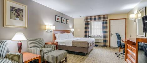 A hotel room with a bed, two striped armchairs, a small table, a desk with a chair, a dresser, and a mirror.