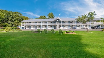 A two-story motel with a large lawn, outdoor seating area, and multiple cars parked in front.