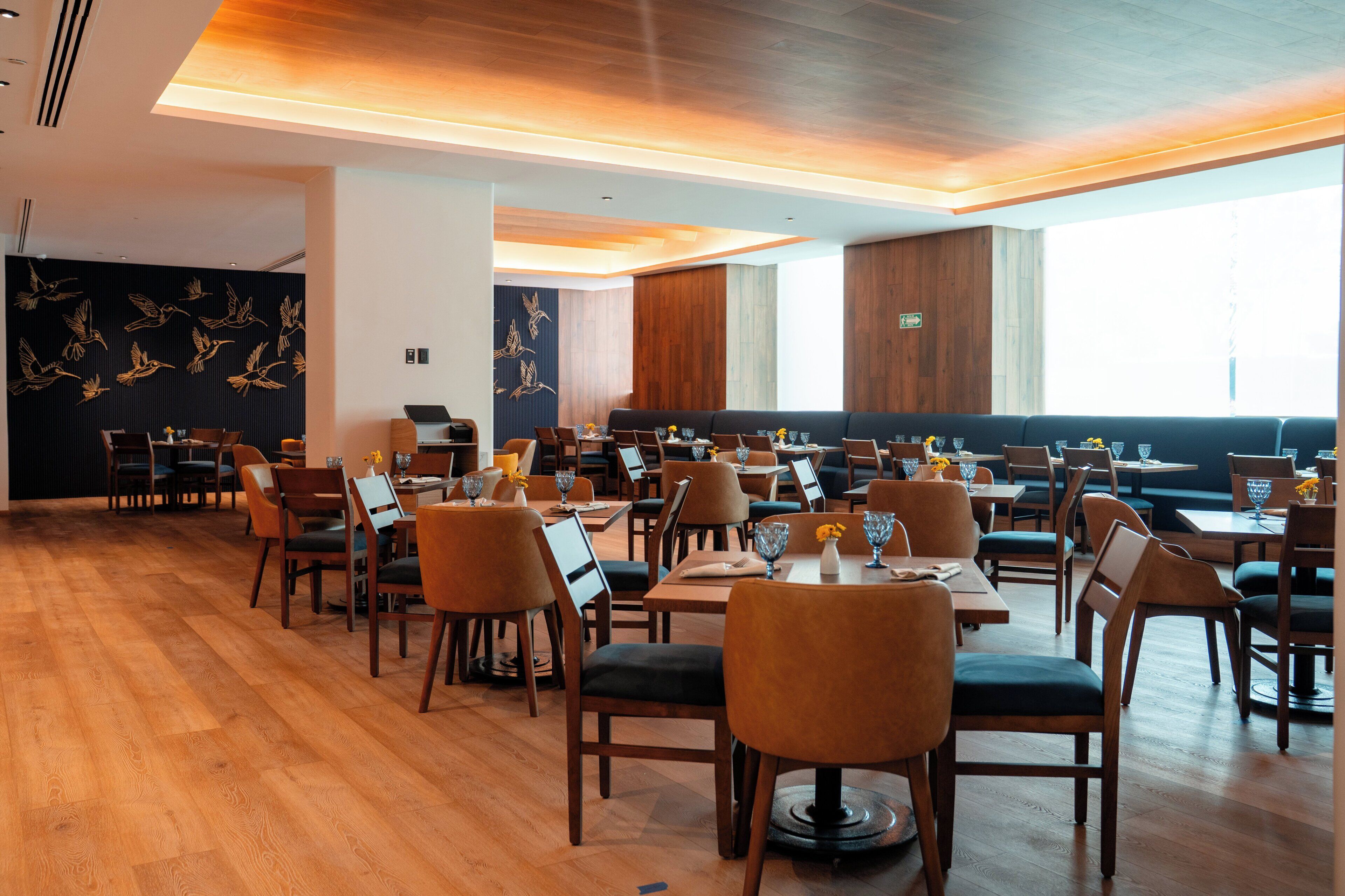 Un restaurante con varias mesas y sillas, suelo de madera y una pared decorada con un mural de aves.