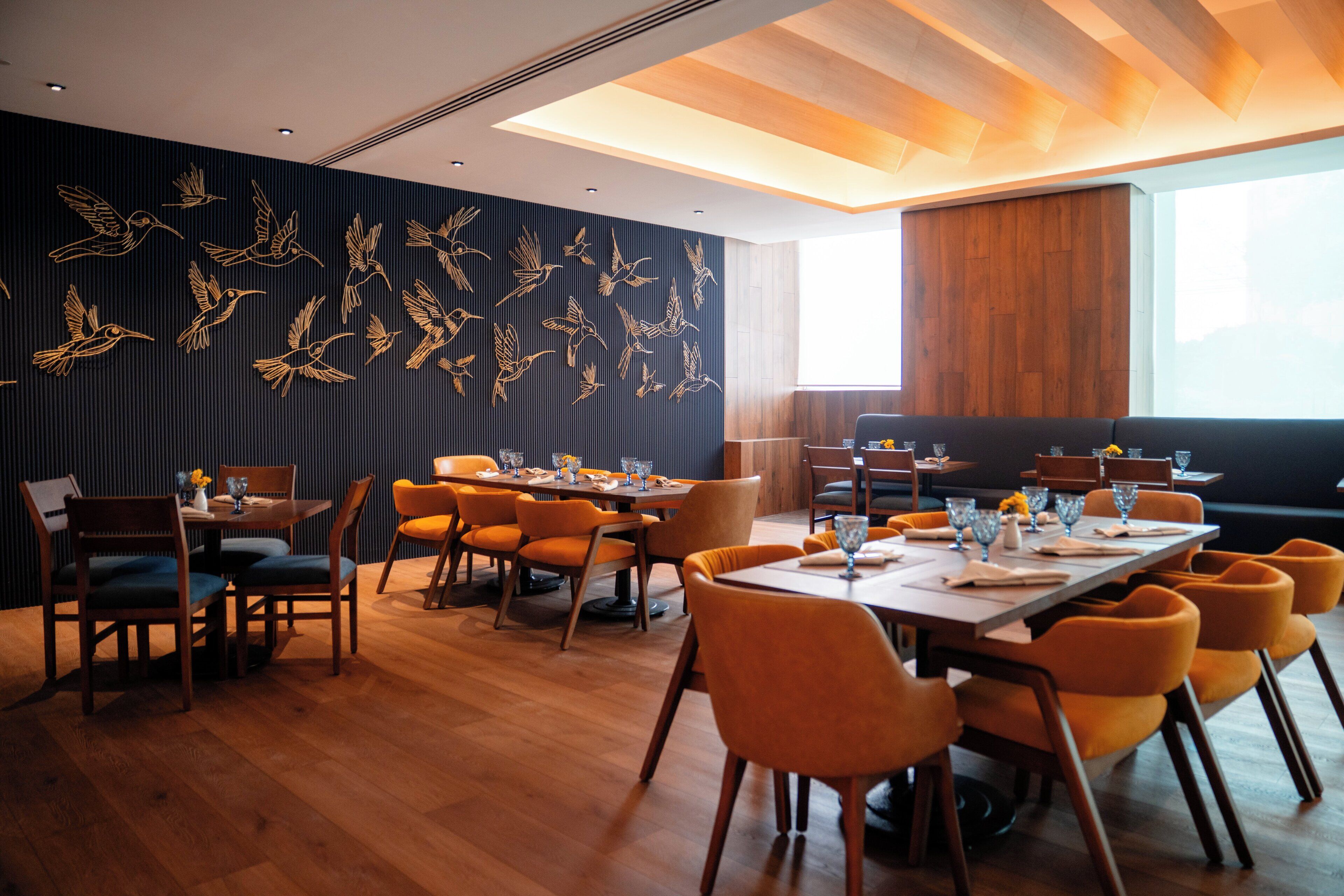 A modern dining area with wooden floors, orange chairs, and a long table set for dining.