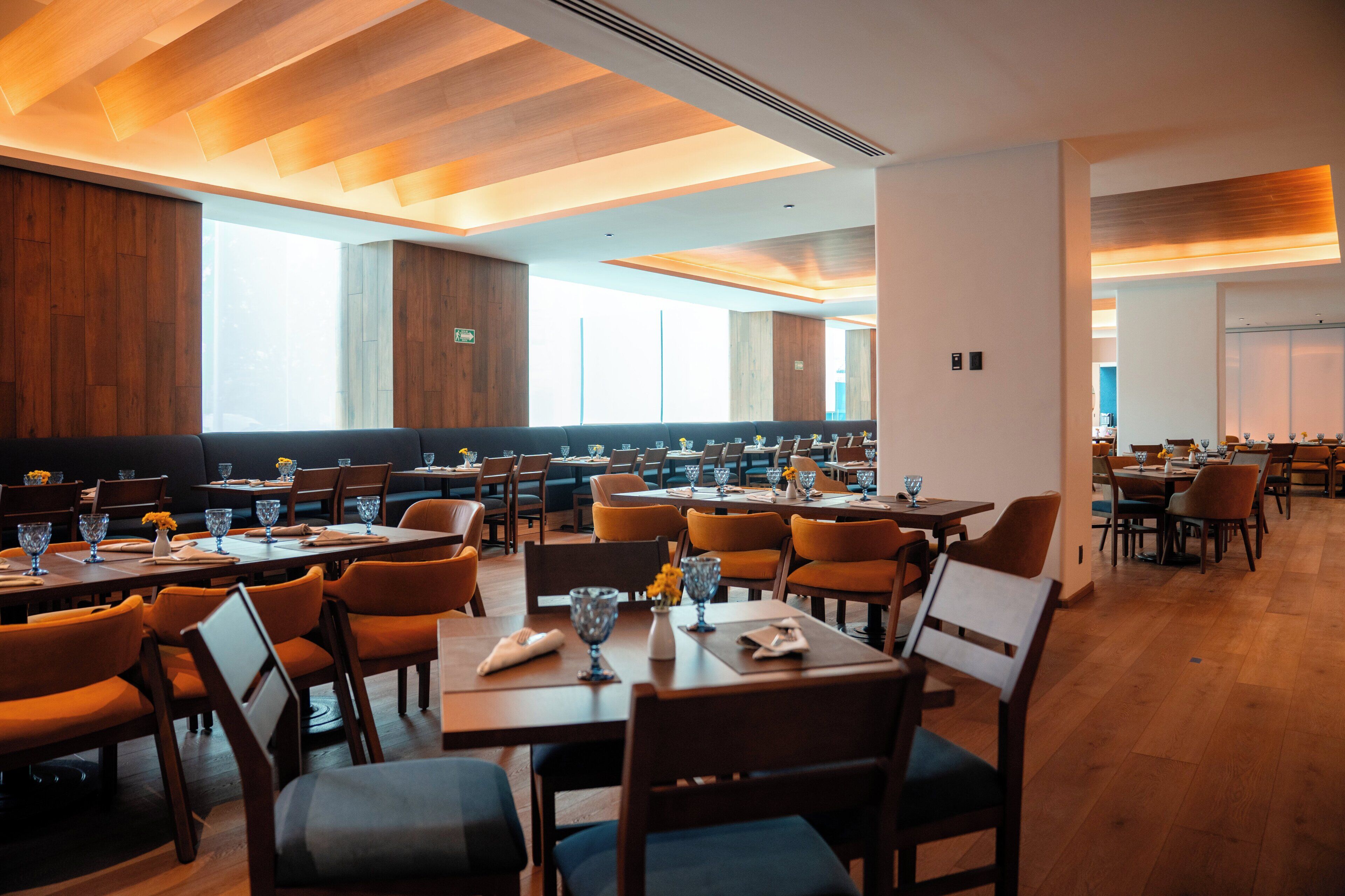 A spacious restaurant with multiple dining tables and chairs, large windows allowing natural light, and a modern interior design.