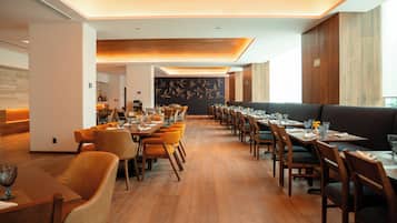 A modern dining area with long tables, wooden chairs, and a central wall with a bird mural.