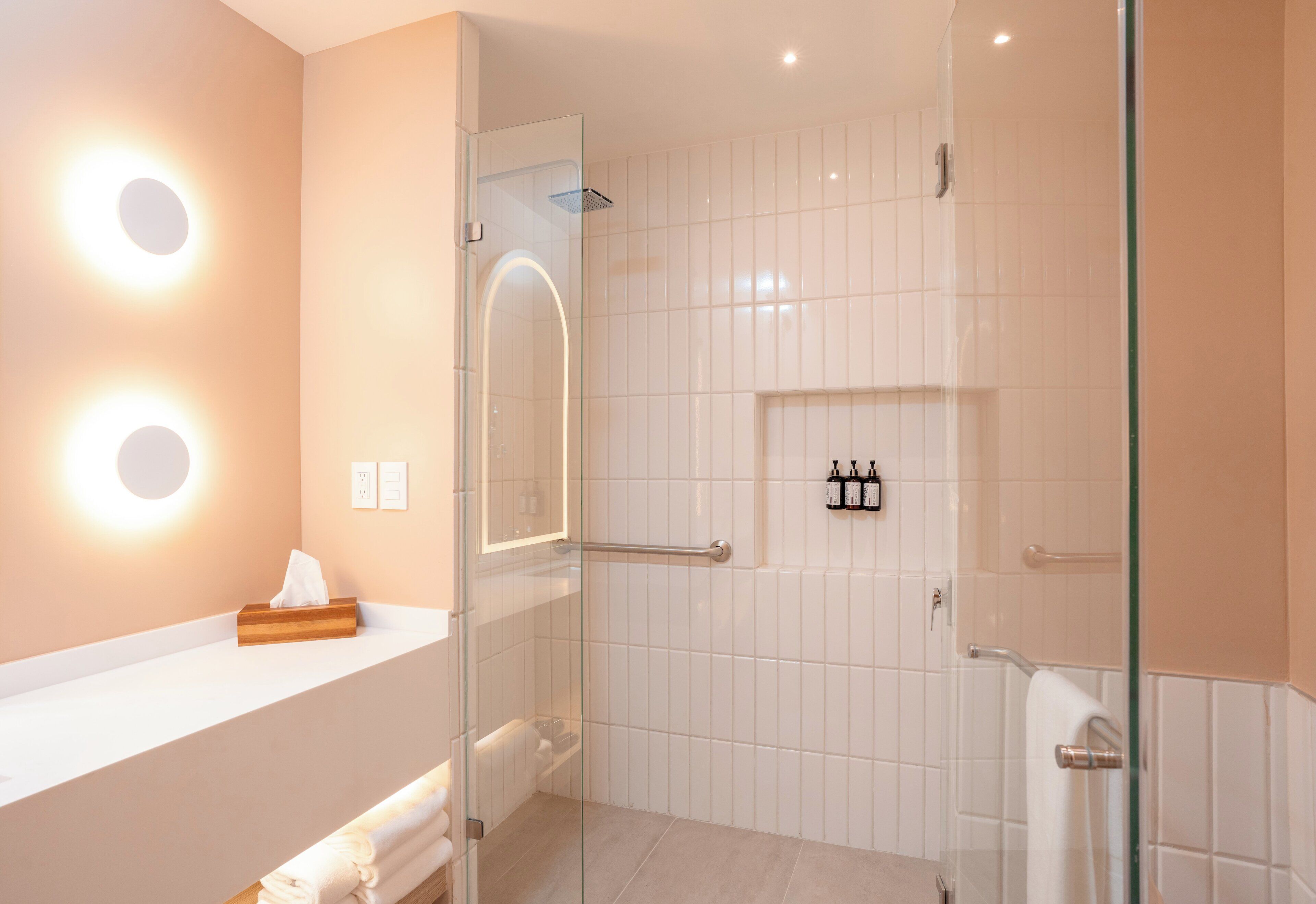 Une salle de bain moderne avec une douche à parois de verre, un mur recouvert de carreaux blancs et un meuble-lavabo doté d’un porte-serviettes.