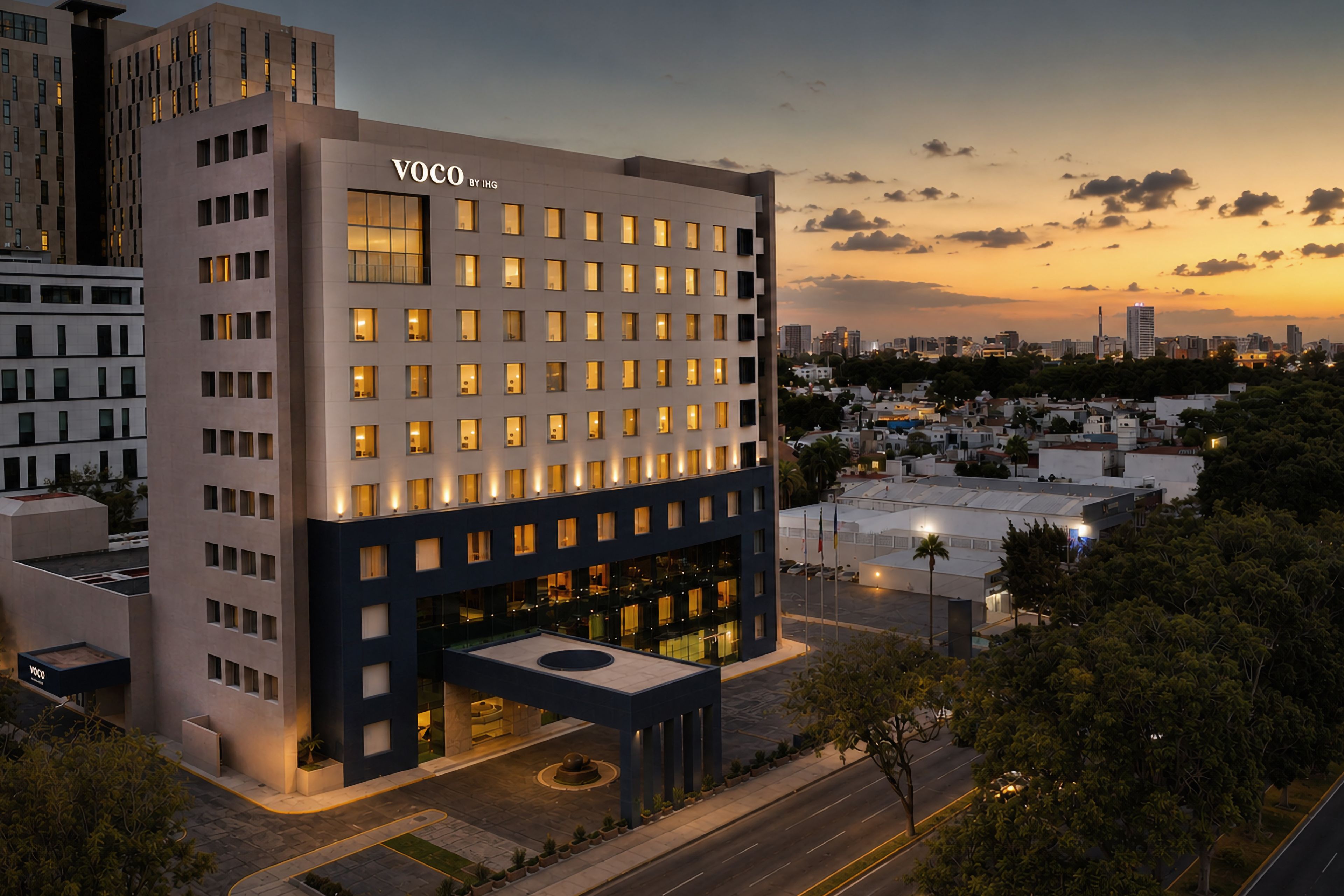 Un hôtel moderne, avec une enseigne bien visible, de nombreuses fenêtres et un espace d’entrée aménagé avec des éléments paysagers.