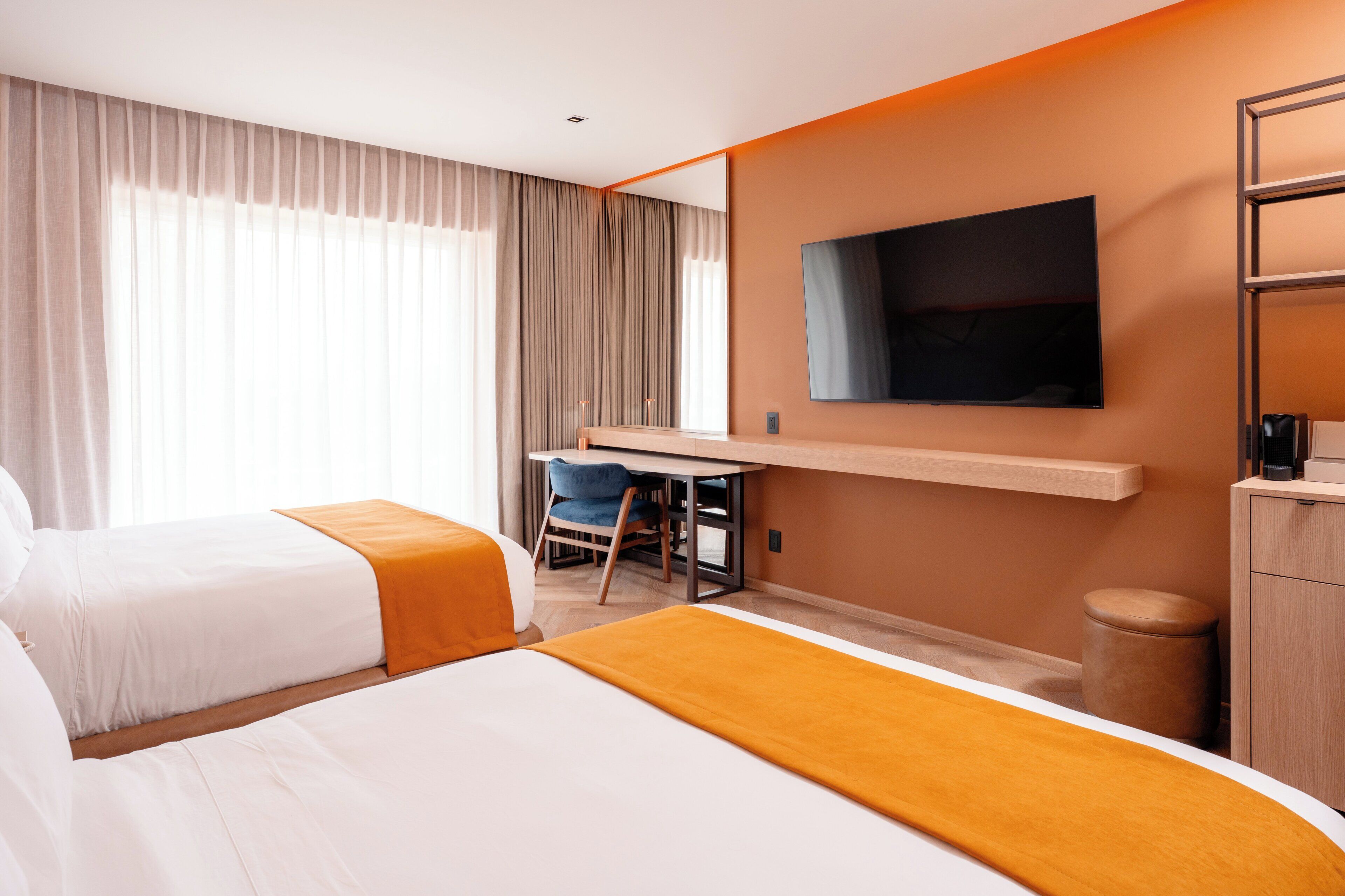 A hotel room with two beds, a desk, a chair, a television, and a wardrobe.