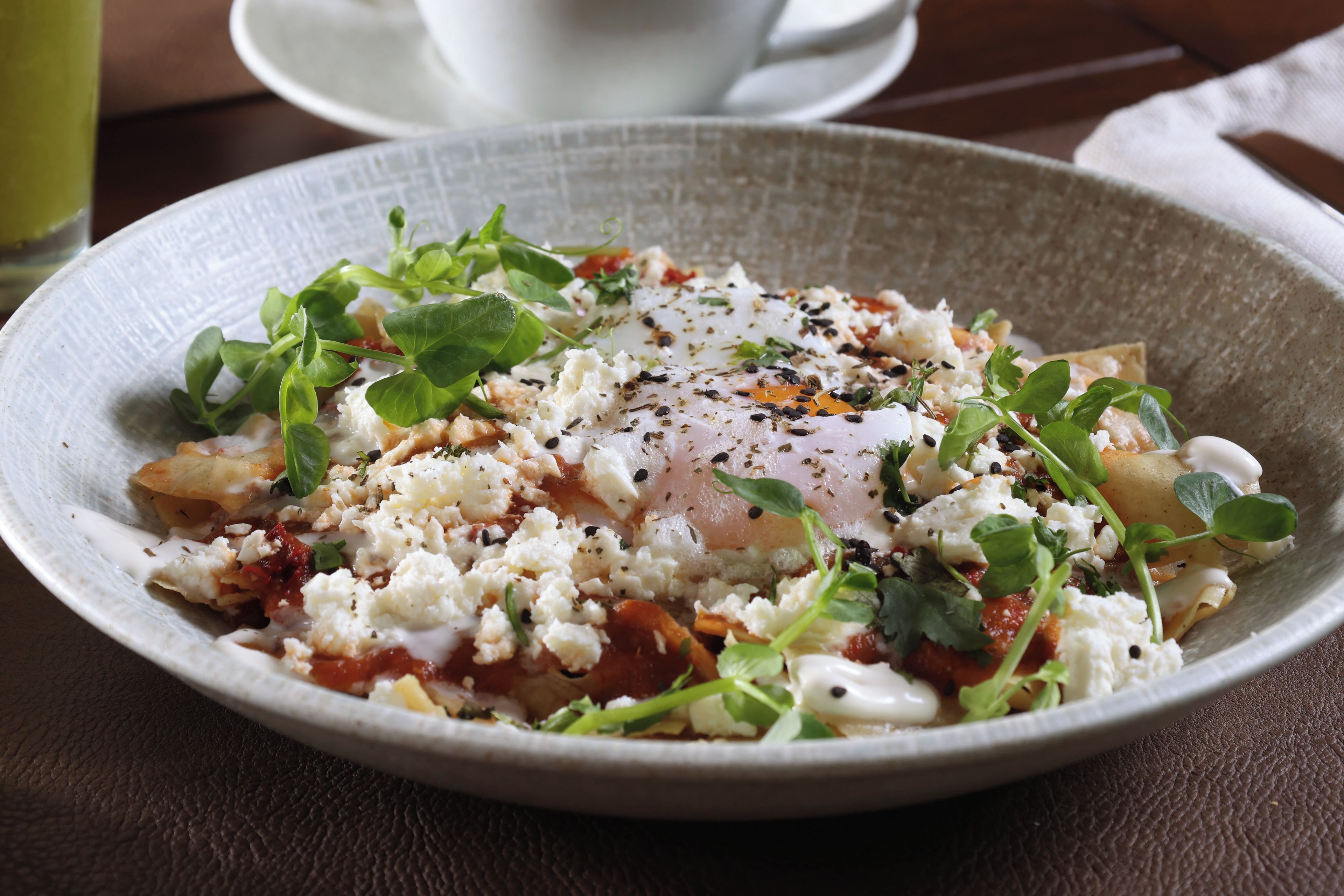 A plate of food with a poached egg, feta cheese, and greens on a textured plate.