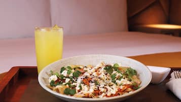 A plate of pasta with greens and cheese, a glass of yellow drink, and a fork on a wooden tray.