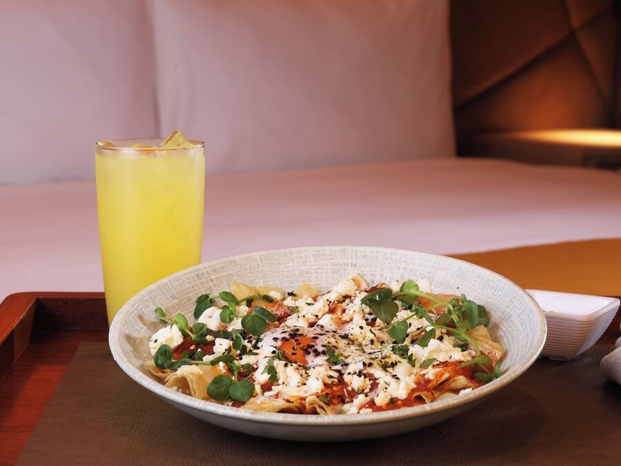 A plate of pasta with greens and cheese, a glass of yellow drink, and a fork on a wooden tray.