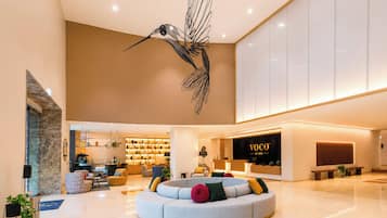 Un moderno vestíbulo de hotel con un área de estar central, una recepción y una escultura decorativa de un pájaro.