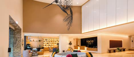 Un moderno vestíbulo de hotel con un área de estar central, una recepción y una escultura decorativa de un pájaro.