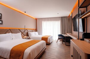 A hotel room with two beds, a desk, a chair, a TV, and a large window with curtains.