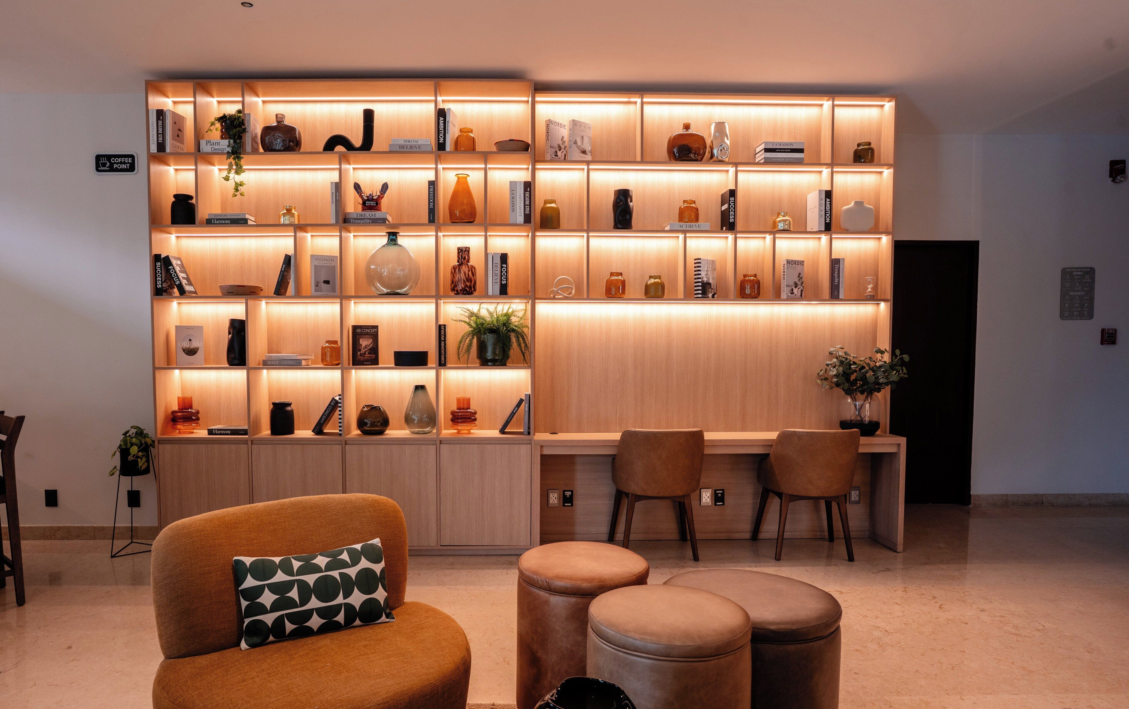 A modern living room with a wooden bookshelf, a coffee point sign, and a seating area with a sofa and ottomans.