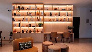 A modern living room with a wooden bookshelf, a coffee point sign, and a seating area with a sofa and ottomans.