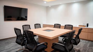 A conference room with a large table, six chairs, a flat-screen TV, and a kitchenette area.