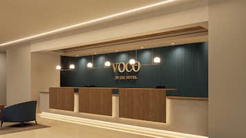 A reception desk with a dark blue wall, wooden panels, and a sign reading 'Voco An IHG Hotel'.