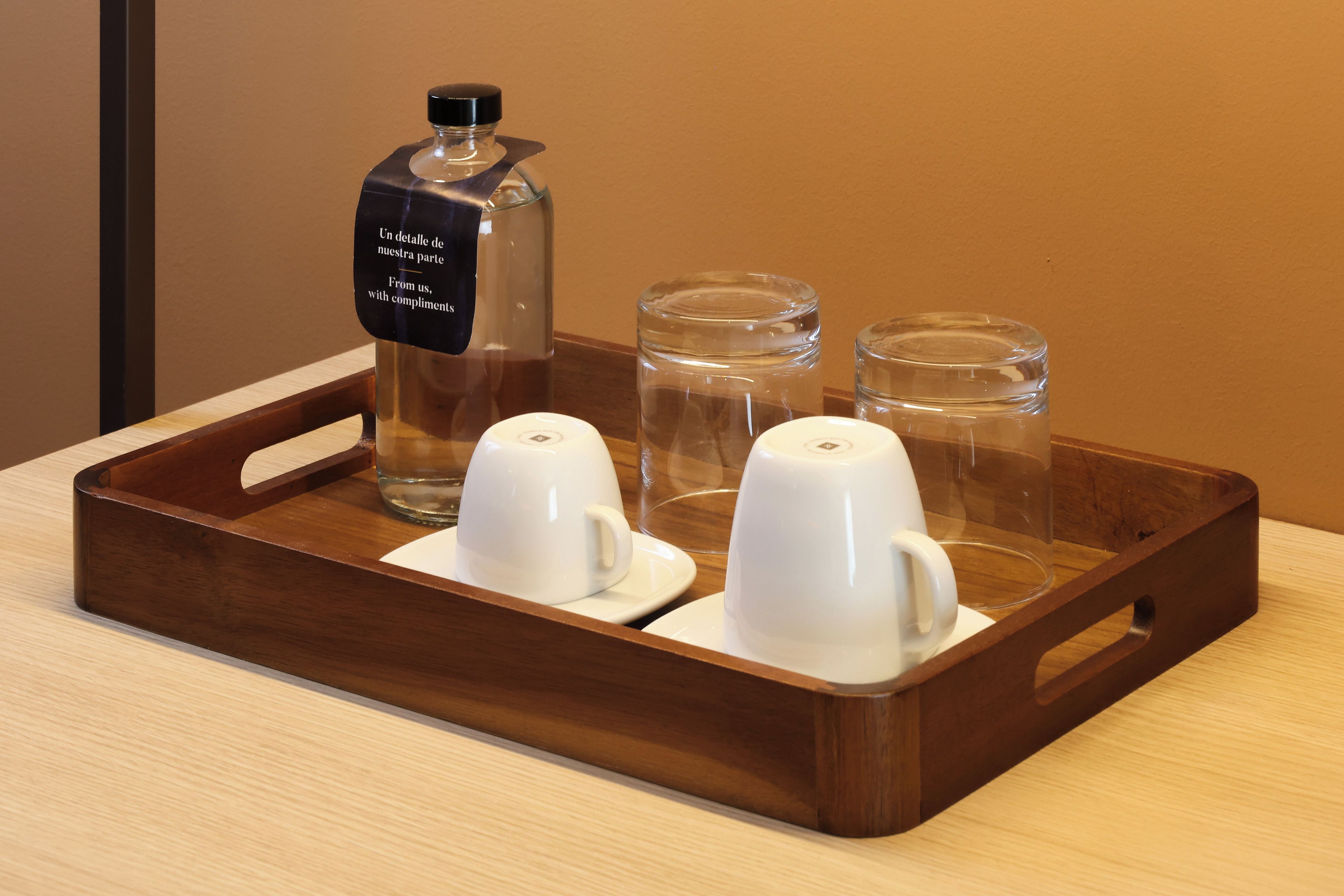 Una bandeja con una botella, dos tazas y dos vasos sobre una superficie de madera.