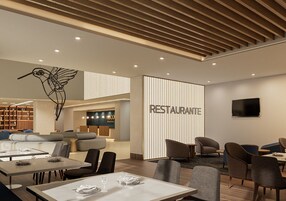 Un interior de restaurante moderno con zona de comedor, sofás y un televisor montado en la pared.