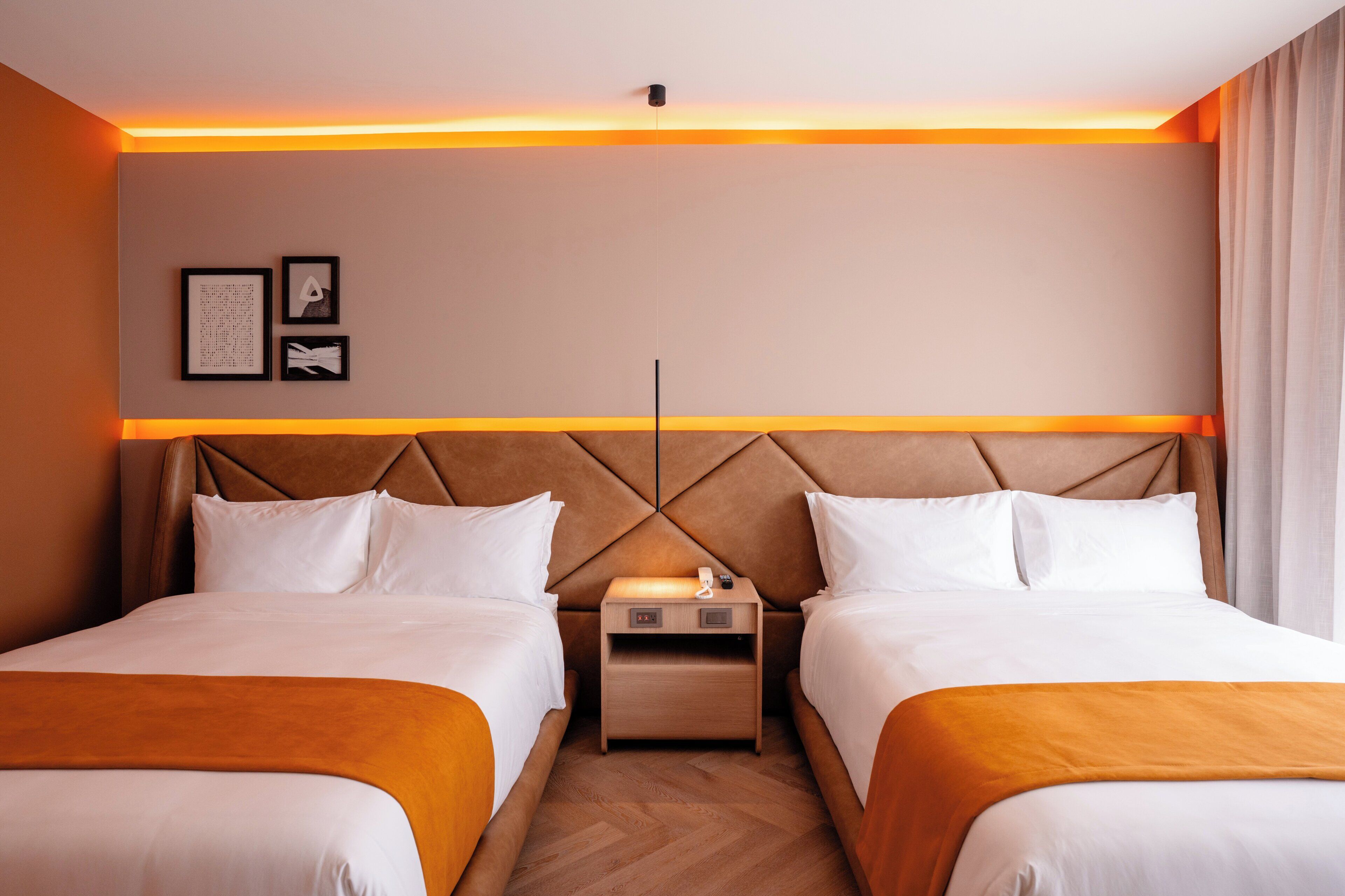 A hotel room with two beds, a nightstand, and a wall-mounted light fixture.