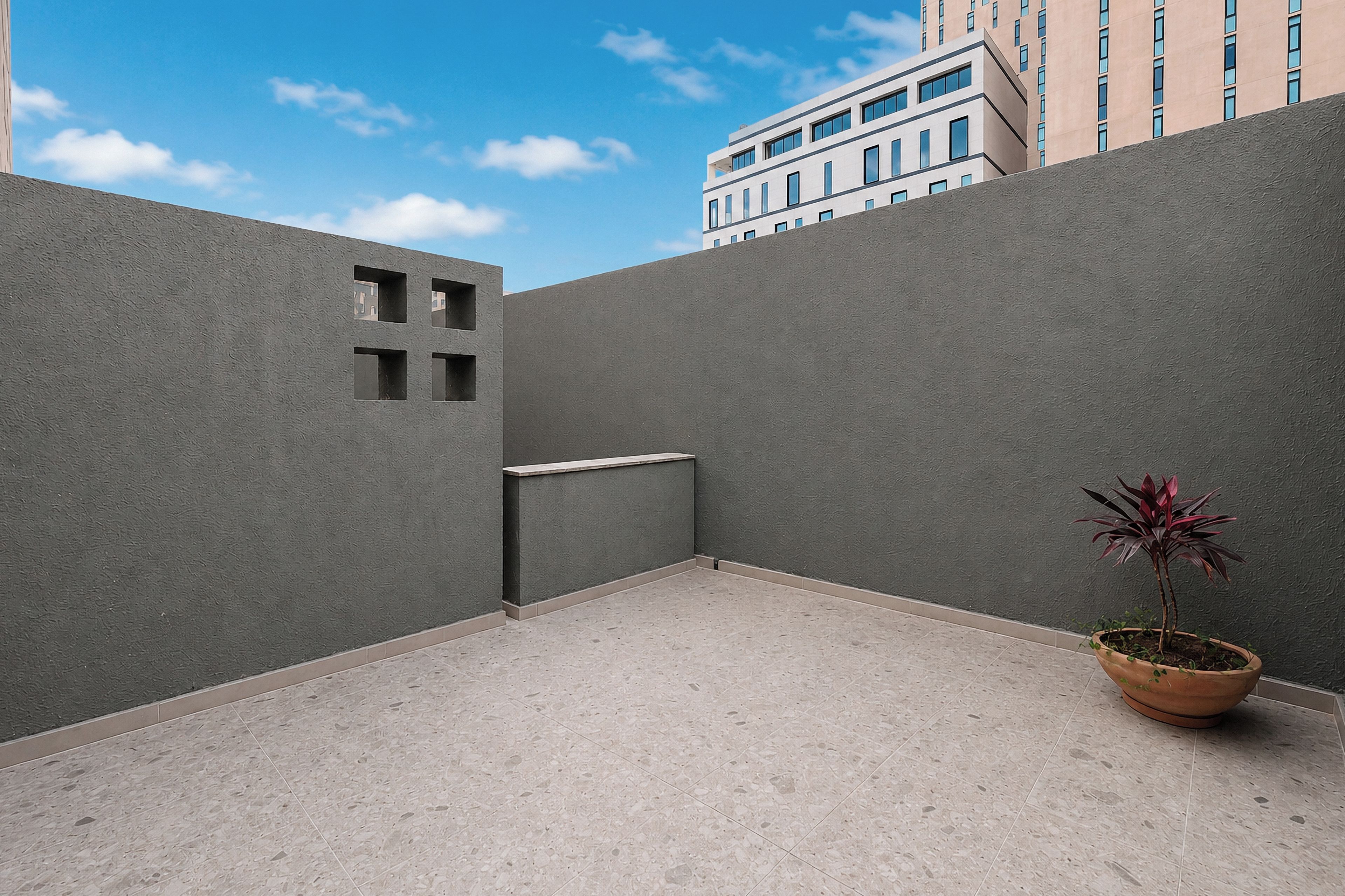 A modern outdoor space with a grey wall, a small planter with a plant, and a tiled floor.