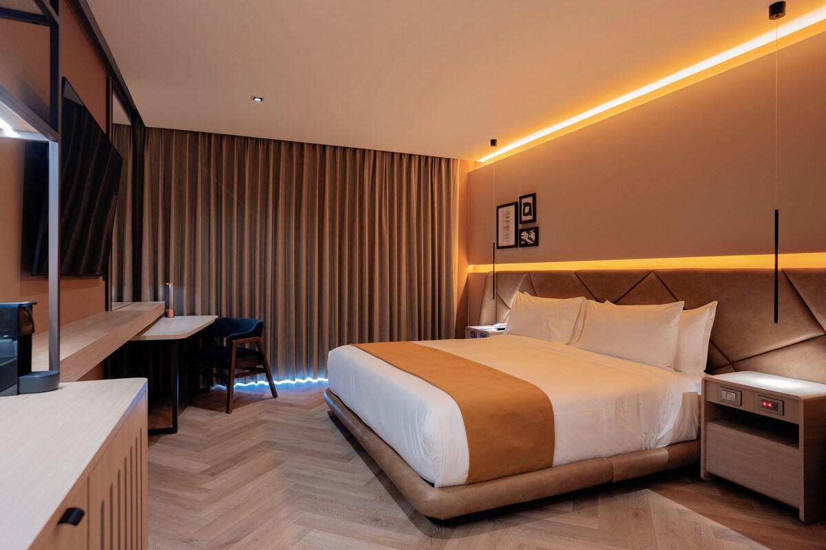 A modern hotel room with a bed, desk, chair, and a nightstand.