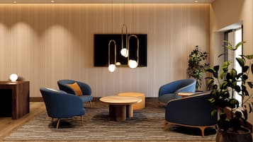 Un salon moderne avec un téléviseur à écran plat, deux fauteuils bleus, une table basse ronde en bois et un luminaire suspendu.