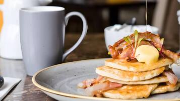 Un plato de panqueques con tocino y un trozo de mantequilla, acompañado por una taza.