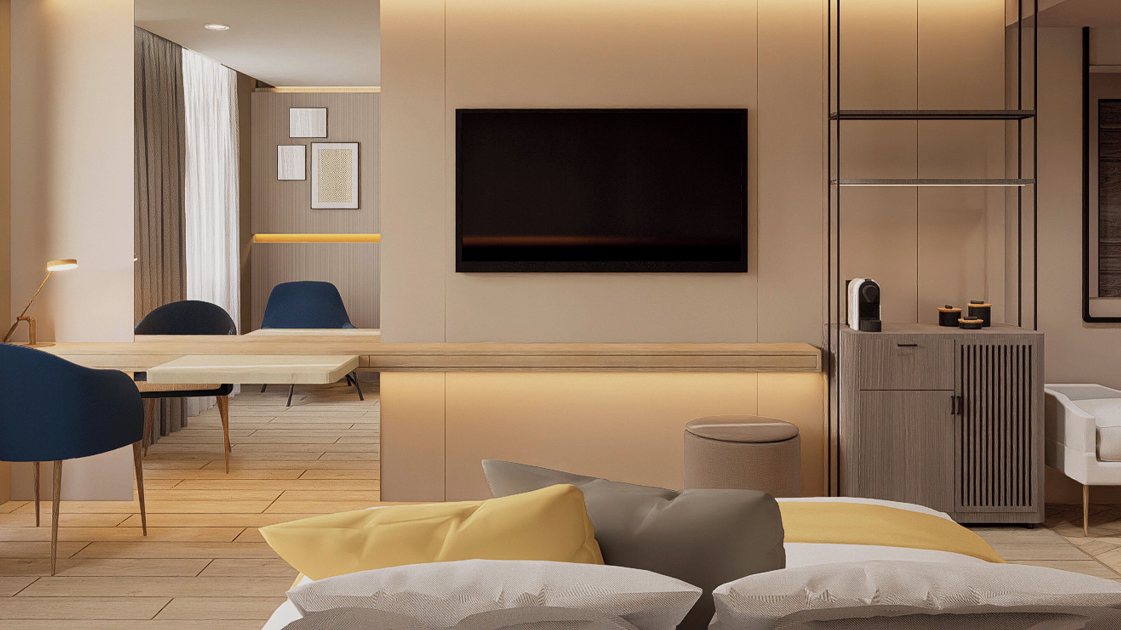 A modern hotel room with a flat-screen TV mounted on the wall, a desk with chairs, a sofa with cushions, and a cabinet with a mirror.