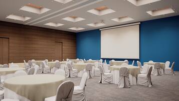 A conference room with round tables, chairs, a projector screen, and a blue accent wall.