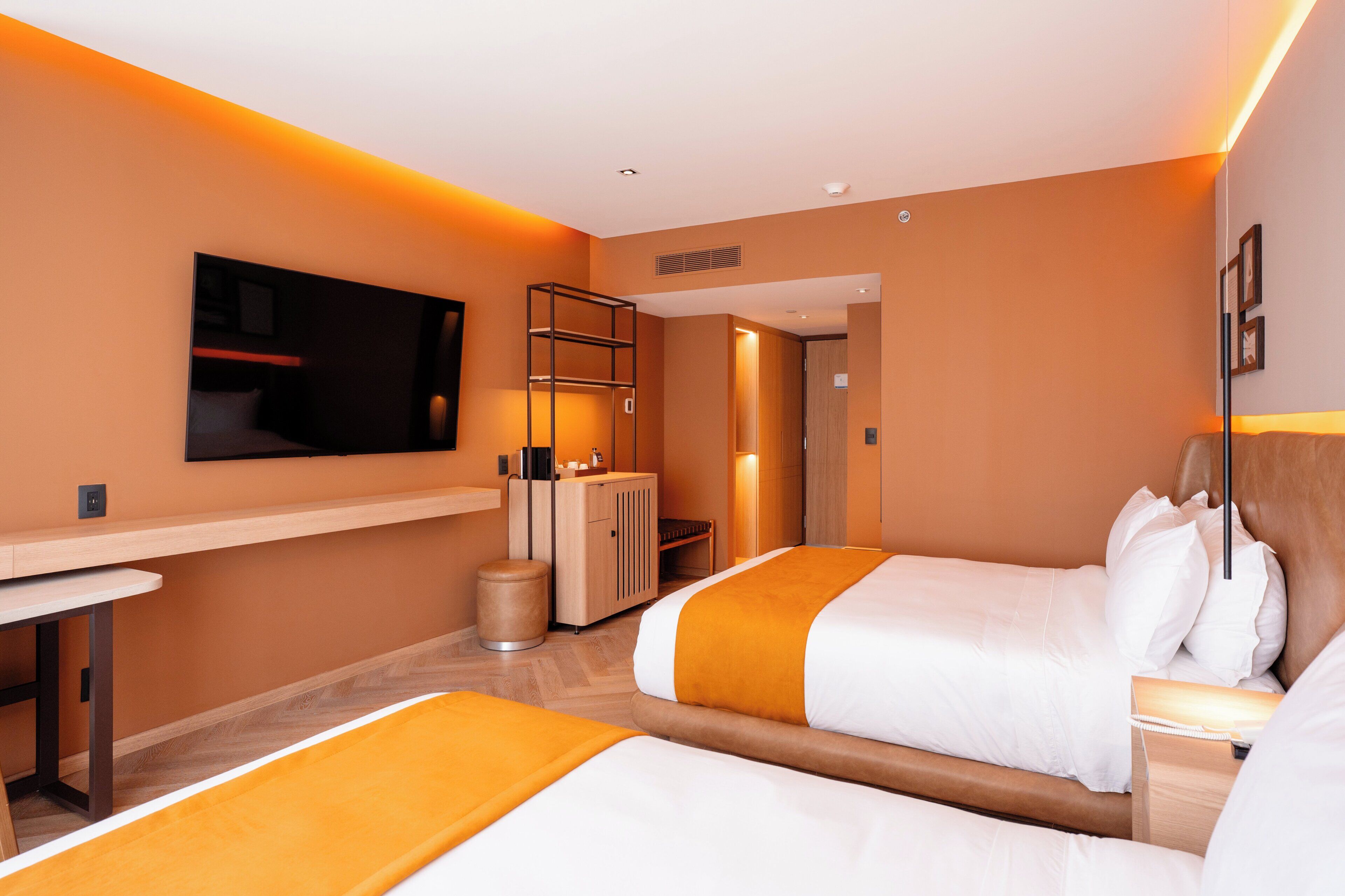 Ein Hotelzimmer mit zwei Betten, einem Schreibtisch, einer Minibar und einem Fernseher.