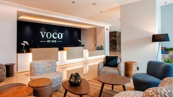 Een moderne lobby met zitplaatsen, een receptiebalie en een muur met de tekst 'Voco by IHG'.