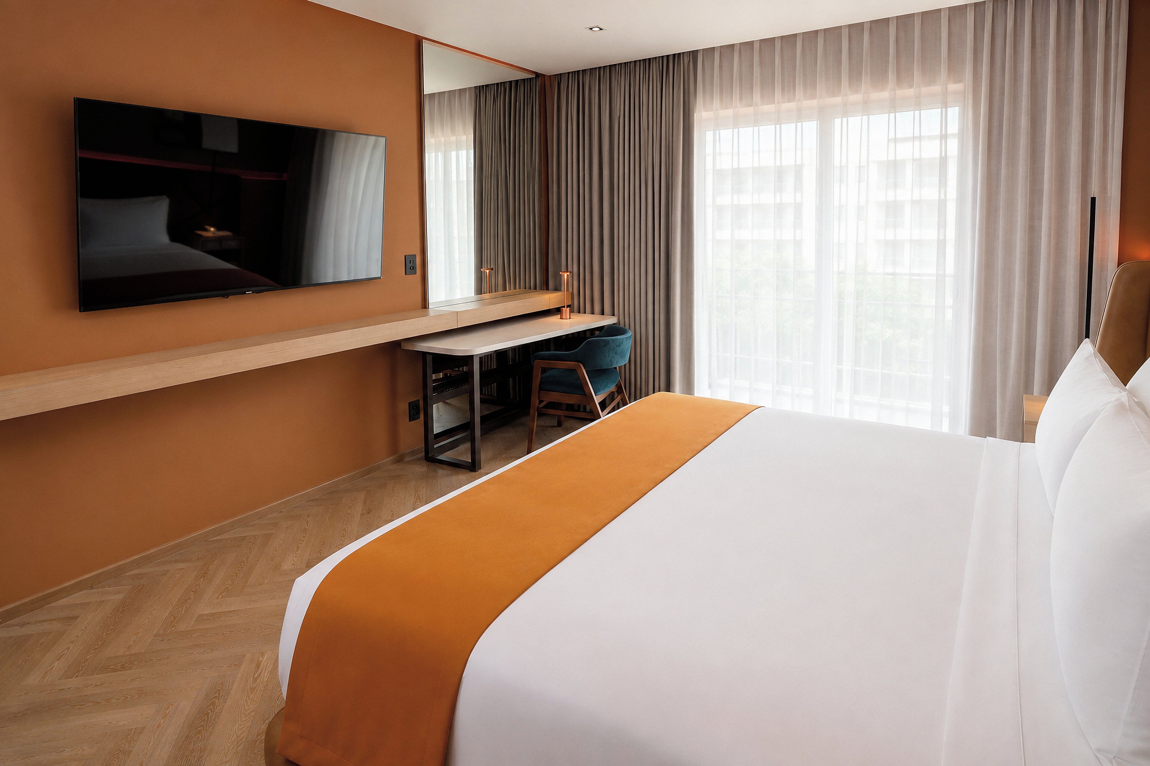 A hotel room with a bed, a desk, a chair, a television, and a window with curtains.
