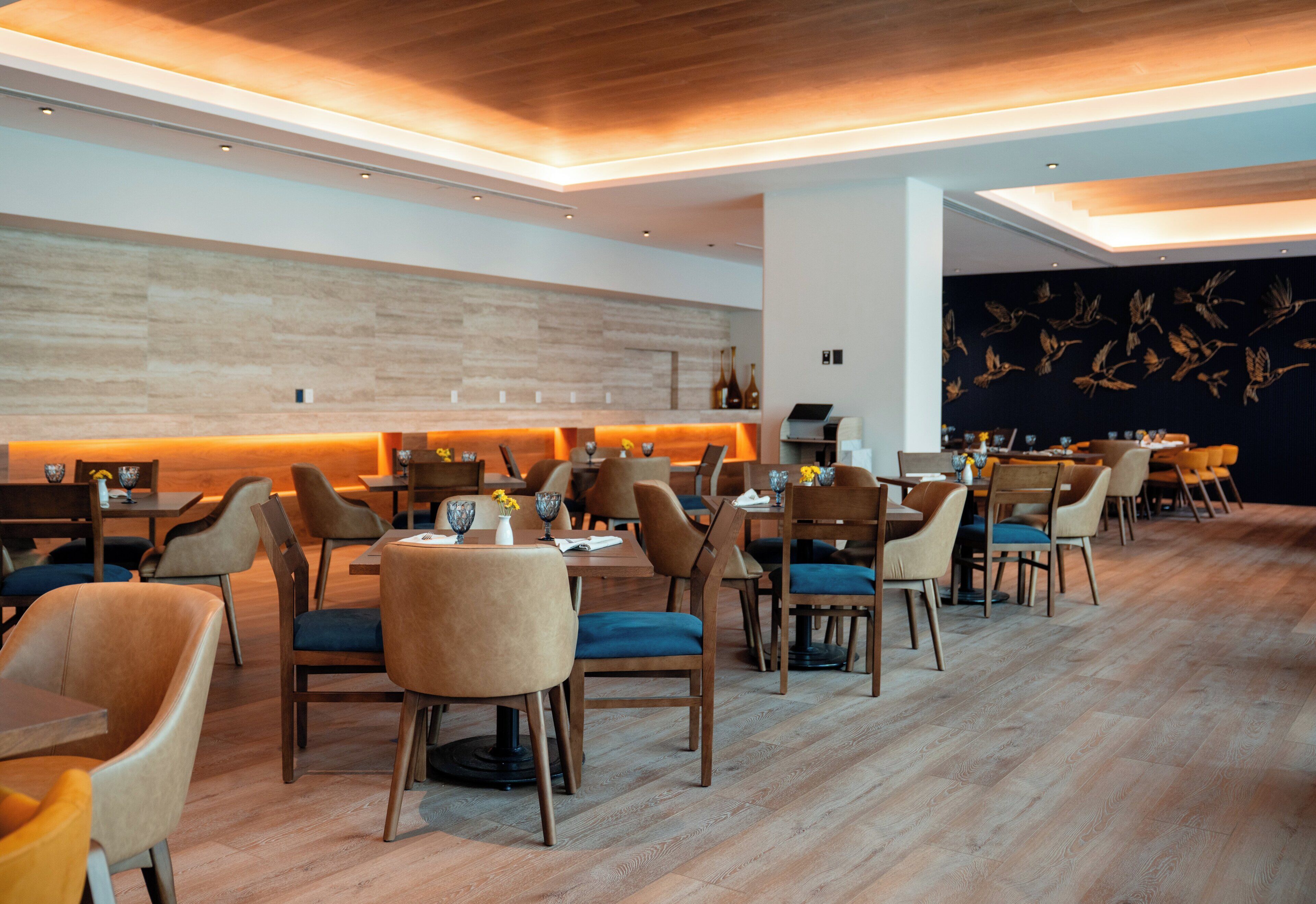 A modern restaurant with wooden flooring, upholstered chairs, and a long counter with tables.